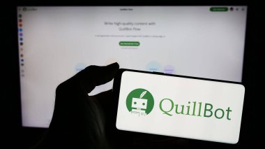 Stuttgart, Almanya - 03-12-2024: Üzerinde Amerikan Yapay Zeka Yazı Şirketi QuillBot 'un logosu olan mobil pofon tutan kişi web sayfasının önünde. Telefon ekranına odaklan.