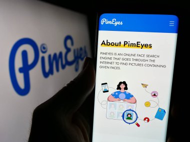 Stuttgart, Germany - 03-13-2024: Person holding cellphone with webpage of facial recognition search company PimEyes in front of business logo. Focus on center of phone display. clipart