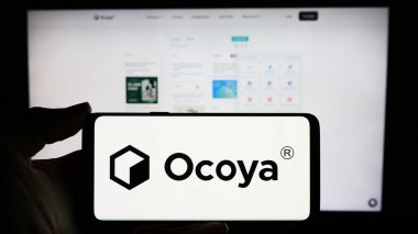 Stuttgart, Almanya - 03-13-2024: Litvanyalı yapay zeka şirketi Ocoya 'nın logosuna sahip cep telefonu sahibi kişi iş sayfasının önünde. Telefon ekranına odaklan.