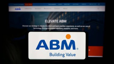 Stuttgart, Almanya - 03-13-2024: ABD tesis yönetimi şirketi ABM Industries Inc. 'in logosuyla cep telefonu sahibi kişi iş sayfasının önünde. Telefon ekranına odaklan.