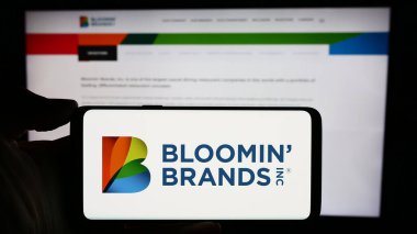 Stuttgart, Almanya - 03-13-2024: ABD 'li restoran holding şirketi Bloomin' Brand Inc. 'in logosuyla cep telefonu sahibi kişi iş sayfasının önünde. Telefon ekranına odaklan.