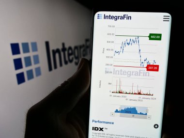 Stuttgart, Almanya - 03-20-2024: İngiliz finans şirketi IntegraFin Holding plc 'nin web sitesi ile logo önünde akıllı telefon tutan kişi. Telefon ekranının merkezine odaklan.