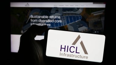 Stuttgart, Almanya - 03-20-2024: İngiliz yatırım şirketi HICL Altyapı 'nın logosuna sahip cep telefonu sahibi kişi iş sayfasının önünde. Telefon ekranına odaklan.