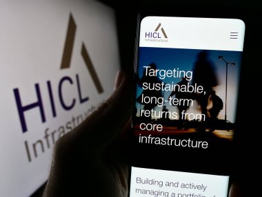 Stuttgart, Almanya - 03-20-2024: İngiliz yatırım şirketi HICL Altyapı 'nın logo önündeki web sayfası ile cep telefonu tutan kişi. Telefon ekranının merkezine odaklan.
