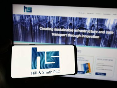 Stuttgart, Almanya - 03-20-2024: İngiliz altyapı şirketi Hill ve Smith plc 'in logosuna sahip akıllı telefon sahibi kişi web sitesinin önünde. Telefon ekranına odaklan.