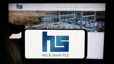 Stuttgart, Almanya - 03-20-2024: İngiliz altyapı şirketi Hill ve Smith plc 'in logosunun bulunduğu cep telefonu sahibi kişi iş sayfasının önünde. Telefon ekranına odaklan.