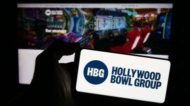 Stuttgart, Almanya - 03-20-2024: İngiliz bowling şirketi Hollywood Bowl Group plc 'un logosuna sahip akıllı telefon sahibi kişi web sitesinin önünde. Telefon ekranına odaklan.