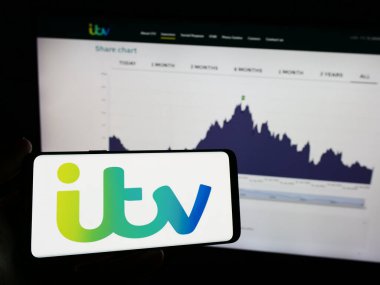 Stuttgart, Almanya - 03-23-2024: İngiliz medyasının logosu ve yayın şirketi ITV plc 'nin logosu olan cep telefonunu Business web sayfasının önünde tutan kişi. Telefon ekranına odaklan.