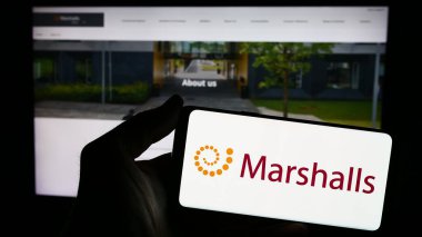 Stuttgart, Almanya - 03-25-2024: Üzerinde İngiliz peyzaj ürünleri şirketi Marshalls plc 'nin logosu bulunan akıllı telefon sahibi kişi web sitesinin önünde. Telefon ekranına odaklan.