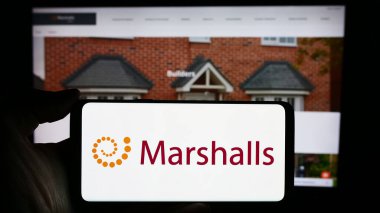 Stuttgart, Almanya - 03-25-2024: Üzerinde İngiliz peyzaj ürünleri şirketi Marshalls plc 'nin logosu bulunan cep telefonu sahibi kişi iş sayfasının önünde. Telefon ekranına odaklan.