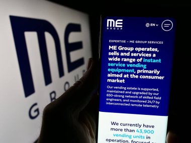 Stuttgart, Almanya - 03-25-2024: İngiliz otomat firması ME Group International plc 'in logolu web sayfası ile akıllı telefon tutan kişi. Telefon ekranının merkezine odaklan.