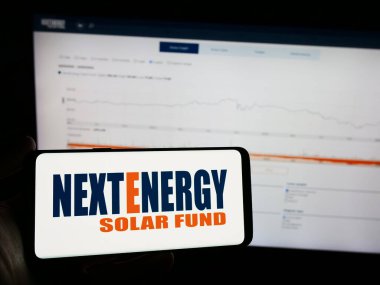 Stuttgart, Almanya - 03-25-2024: Yatırım şirketi NextEnergy Solar Fund Limited 'in logosuna sahip cep telefonu sahibi kişi iş sayfasının önünde. Telefon ekranına odaklan.