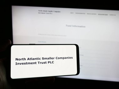 Stuttgart, Almanya - 03-25-2024: Web sitesi önünde üzerinde North Atlantic Small Companies Investment Trust plc logosu bulunan kişi. Telefon ekranına odaklan.