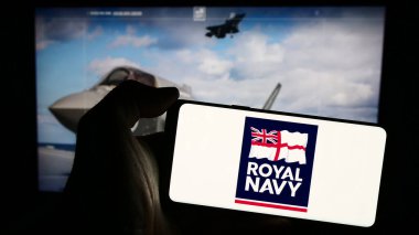 Stuttgart, Germany - 03-25-2024: Person holding smartphone with logo of United Kingdom naval warfare Royal Navy (RN) in front of website. Focus on phone display. clipart