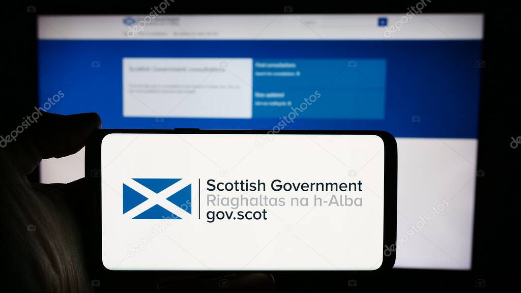 Stuttgart, Germany - 03-25-2024: Person holding mobile phone with logo of Scottish Government (Riaghaltas na h-Alba) in front of web page. Focus on phone display.