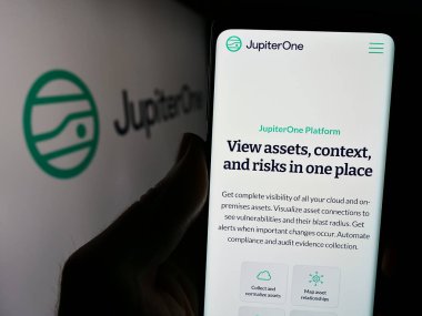 Stuttgart, Almanya - 03-27-2024: Bulut altyapı yönetim şirketi JupiterOne Inc. 'in logolu web sayfası ile akıllı telefon tutan kişi. Telefon ekranının merkezine odaklan.