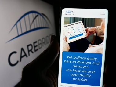 Stuttgart, Almanya - 03-27-2024: ABD 'li sağlık şirketi CareBridge' in web sayfası ile iş logosu önünde cep telefonu tutan kişi. Telefon ekranının merkezine odaklan.