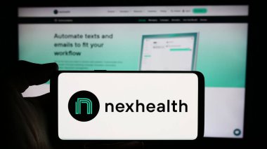 Stuttgart, Almanya - 03-28-2024: ABD 'li sağlık yazılım şirketi NexHealth Inc.' in logosuna sahip cep telefonu sahibi kişi iş sayfasının önünde. Telefon ekranına odaklan.