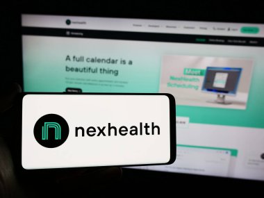 Stuttgart, Almanya - 03-28-2024: İnternet sayfasının önünde Amerikan sağlık yazılım şirketi NexHealth Inc. 'in logosuna sahip cep telefonu sahibi kişi. Telefon ekranına odaklan.