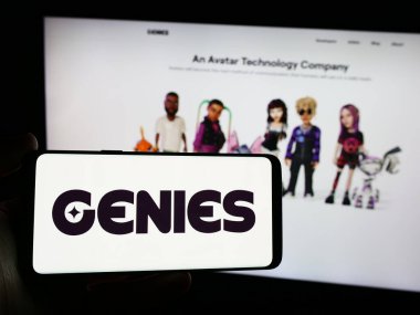 Stuttgart, Germany - 03-28-2024: Person holding smartphone with logo of US avatar technology company Genies Inc. in front of website. Focus on phone display. clipart