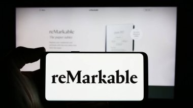 Stuttgart, Almanya - 03-28-2024: İş sayfası önünde Norveçli e-okuyucu şirketi reMarkable AS 'nin logosunu elinde tutan kişi. Telefon ekranına odaklan.