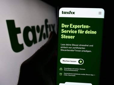 Stuttgart, Almanya - 03-28-2024: Alman vergi yazılım şirketi Taxfix SE 'nin internet sayfası ile akıllı telefon sahibi kişi iş logosu önünde. Telefon ekranının merkezine odaklan.