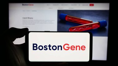 Stuttgart, Almanya - 03-28-2024: ABD 'li biyoteknoloji şirketi Boston Gene Corporation' ın logosuna sahip akıllı telefon sahibi kişi web sitesi önünde. Telefon ekranına odaklan.