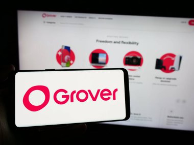 Stuttgart, Germany - 03-28-2024: Person holding smartphone with logo of German consumer electronics rental company Grover in front of website. Focus on phone display. clipart