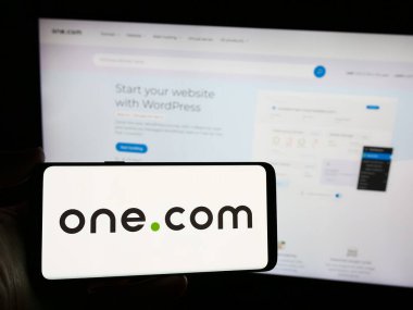 Stuttgart, Almanya - 04-02-2024: Web sunucu şirketi One.com Group 'un logosuna sahip akıllı telefon sahibi kişi web sitesi önünde. Telefon ekranına odaklan.