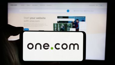 Stuttgart, Almanya - 04-02-2024: İnternet sunucu şirketi One.com Group 'un logosuyla cep telefonu tutan kişi iş sayfası önünde. Telefon ekranına odaklan.