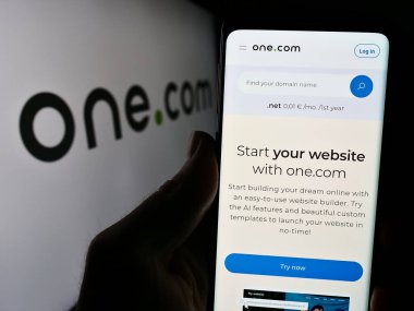 Stuttgart, Almanya - 04-02-2024: İnternet sunucu şirketi One.com Group 'un web sayfası ile birlikte iş logosu önünde cep telefonu tutan kişi. Telefon ekranının merkezine odaklan.