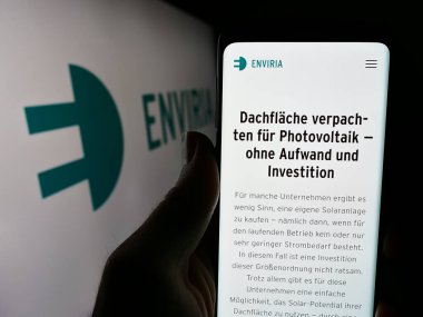 Stuttgart, Almanya - 04-02-2024: Alman güneş enerjisi şirketi ENVIRIA Energy Holding GmbH 'in web sayfası ile logo önünde cep telefonu tutan kişi. Telefon ekranının merkezine odaklan.