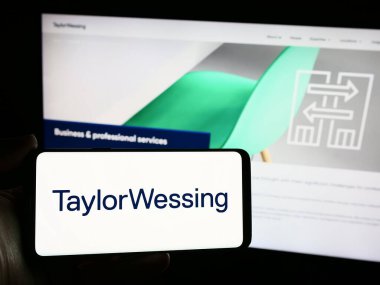Stuttgart, Almanya - 04-02-2024: Uluslararası hukuk firması Taylor Wessing LLLP 'nin logosuna sahip akıllı telefon sahibi kişi web sitesi önünde. Telefon ekranına odaklan.