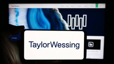 Stuttgart, Germany - 04-02-2024: Person holding cellphone with logo of international law company Taylor Wessing LLP in front of business webpage. Focus on phone display. clipart