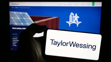 Stuttgart, Germany - 04-02-2024: Person holding mobile phone with logo of international law company Taylor Wessing LLP in front of business web page. Focus on phone display. clipart