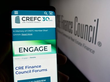 Stuttgart, Germany - 04-04-2024: Person holding cellphone with webpage of trade association CRE Finance Council (CREFC) in front of logo. Focus on center of phone display. clipart