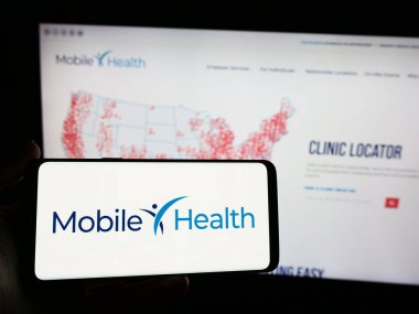 Stuttgart, Almanya - 04-04-2024: İnternet sitesi önünde üzerinde Mobil Sağlık Yönetim Hizmetleri Şirketi logosu olan akıllı telefon sahibi kişi. Telefon ekranına odaklan.