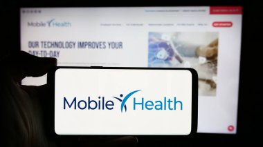 Stuttgart, Almanya - 04-04-2024: ABD 'li Mobile Health Management Services Inc.' in logosuyla cep telefonu sahibi kişi iş sayfasının önünde. Telefon ekranına odaklan.