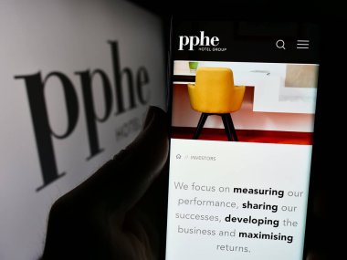 Stuttgart, Almanya - 04-04-2024: İngiliz konukseverlik şirketi PPHE Hotel Group Limited 'in web sayfası ile logo önünde cep telefonu tutan kişi. Telefon ekranının merkezine odaklan.