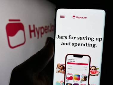Stuttgart, Almanya - 04-07-2024: İngiliz finans teknoloji şirketi HyperJar Limited 'in internet sayfası ile cep telefonu tutan kişi logolu. Telefon ekranının merkezine odaklan.