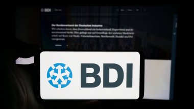 Stuttgart, Germany - 04-07-2024: Person holding cellphone with logo of Bundesverband der Deutschen Industrie e.V. (BDI) in front of webpage. Focus on phone display. clipart