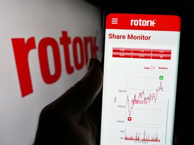 Stuttgart, Germany - 04-07-2024: Person holding cellphone with webpage of British flow control equipment company Rotork plc in front of logo. Focus on center of phone display. clipart