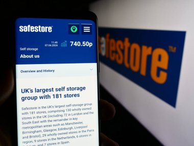 Stuttgart, Almanya - 04-07-2024: İngiliz depolama şirketi Safestore Holding plc 'nin web sayfası ile logo önünde cep telefonu tutan kişi. Telefon ekranının merkezine odaklan.