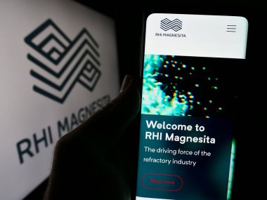Stuttgart, Almanya - 04-07-2024: Refraktör ürünler şirketi RHI Magnesita NV 'nin web sayfası ile logo önünde cep telefonu tutan kişi. Telefon ekranının merkezine odaklan.