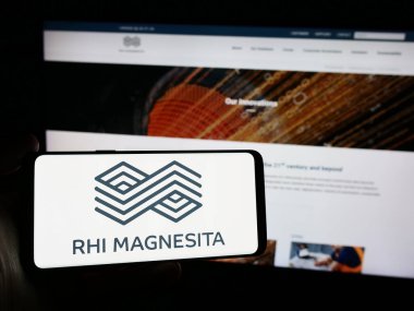 Stuttgart, Germany - 04-07-2024: Person holding smartphone with logo of refractory products company RHI Magnesita N.V. in front of website. Focus on phone display. clipart