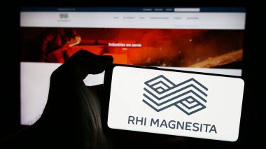 Stuttgart, Germany - 04-07-2024: Person holding mobile phone with logo of refractory products company RHI Magnesita NV in front of business web page. Focus on phone display. clipart