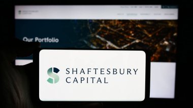 Stuttgart, Almanya - 04-08-2024: İngiliz yatırım şirketi Shaftesbury Capital plc 'nin logosuyla cep telefonu sahibi kişi iş sayfasının önünde. Telefon ekranına odaklan.