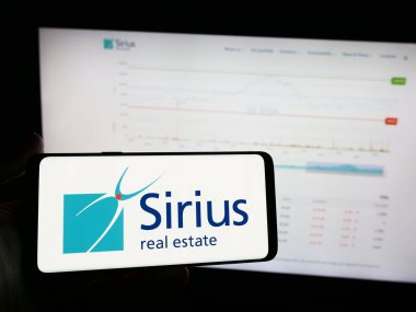 Stuttgart, Almanya - 04-08-2024: Ticari mülkiyet şirketi Sirius Real Estate Limited 'in logosuna sahip cep telefonu sahibi kişi web sayfasının önünde. Telefon ekranına odaklan.