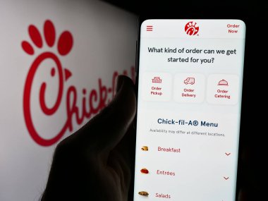 Stuttgart, Almanya - 04-08-2024: ABD 'li fast food restoran şirketi Chick-fil-A Inc.' in logonun önünde cep telefonu tutan kişi. Telefon ekranının merkezine odaklan.