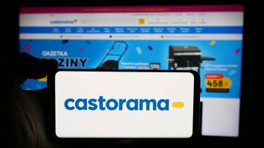 Stuttgart, Germany - 04-08-2024: Person holding cellphone with logo of home improvement store chain company Castorama in front of business webpage. Focus on phone display. clipart